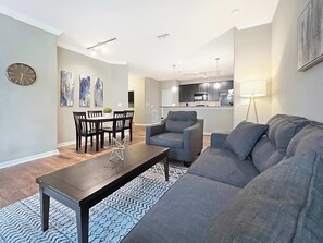 A modern living room with a grey sofa, a wooden coffee table, and a dining area with a dark wooden table and chairs. - Peaceful 2 BR with Private Garage, Prime North Tampa (Lutz)