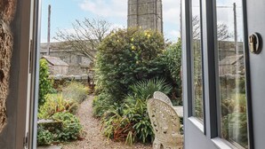 A garden path leading to a white chair, with a stone building and a tower in the background. - Trevrock (Penzance)