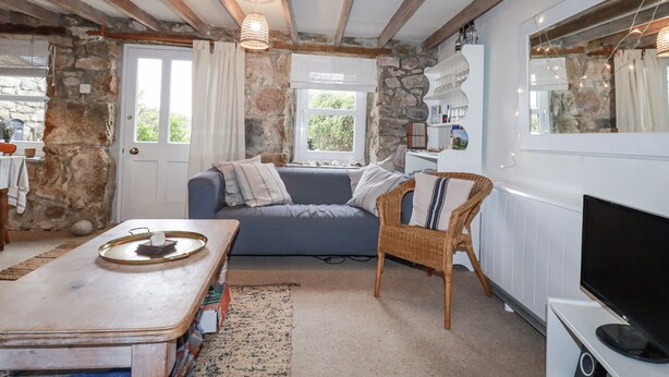 A cozy room with a stone wall, a blue sofa, a wicker chair, a wooden table, and a television. - Trevrock (Penzance)