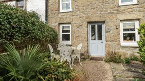 A stone house with a white door, two windows, and a small porch with white chairs. - Trevrock (Penzance)