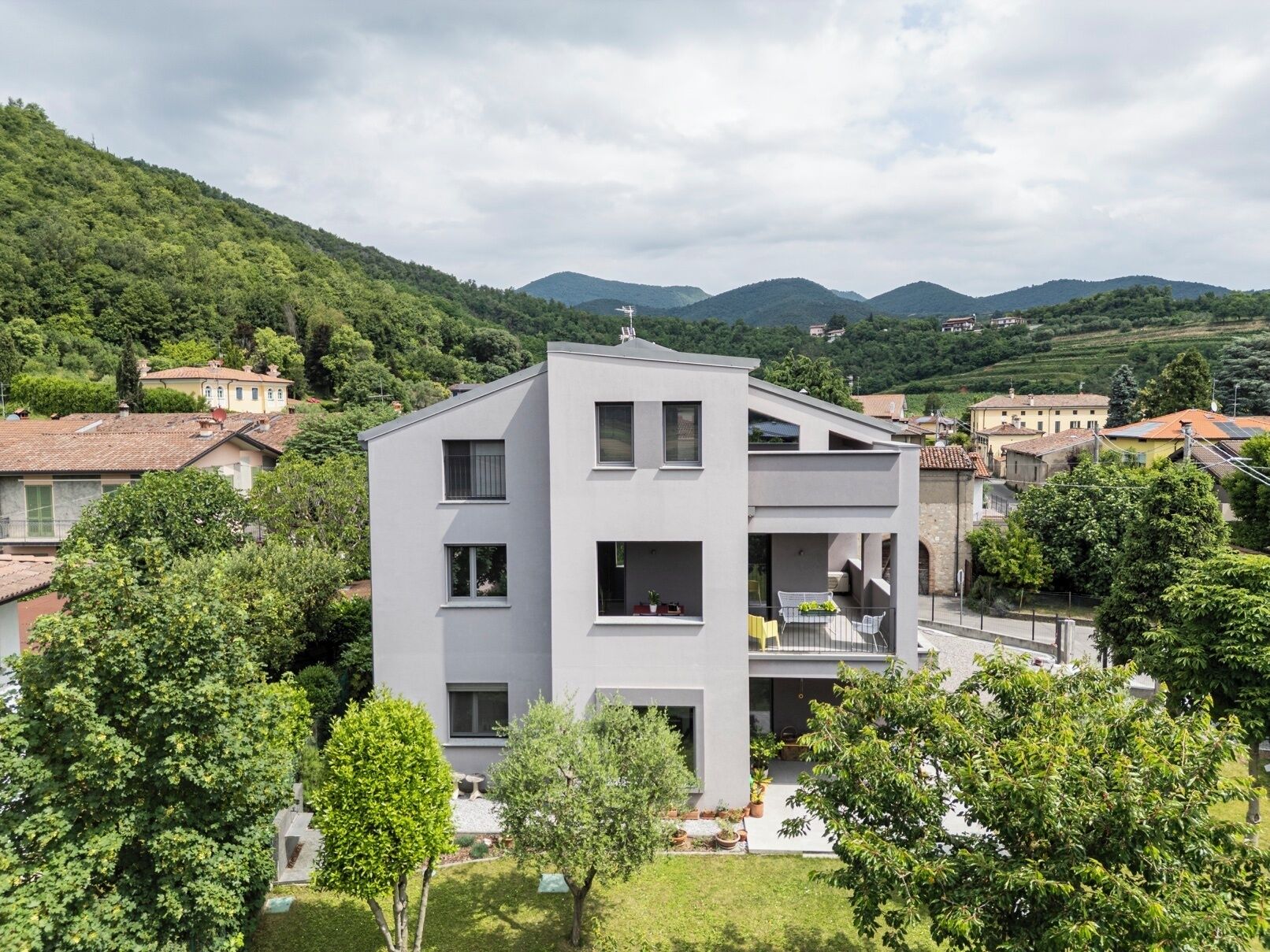 A modern two-story building with a flat roof, surrounded by lush greenery and hills in the background.