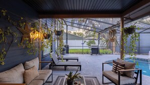 A covered patio with two sofas, hanging plants, and a pool.