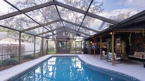 A covered outdoor swimming pool with a glass ceiling, surrounded by a patio area with seating and plants.
