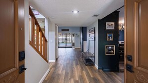 A hallway with wooden flooring, a staircase on the left, and a door on the right.
