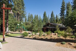 A lodge with a wooden exterior, surrounded by a forested area with a playground and a bell post.