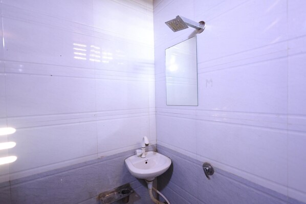 A small bathroom with white tiles, a sink, a mirror, and a showerhead.