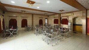 A large conference room with multiple tables and chairs, ceiling fans, and an air conditioning unit. - Hotel Royal Raj (Rajkot)