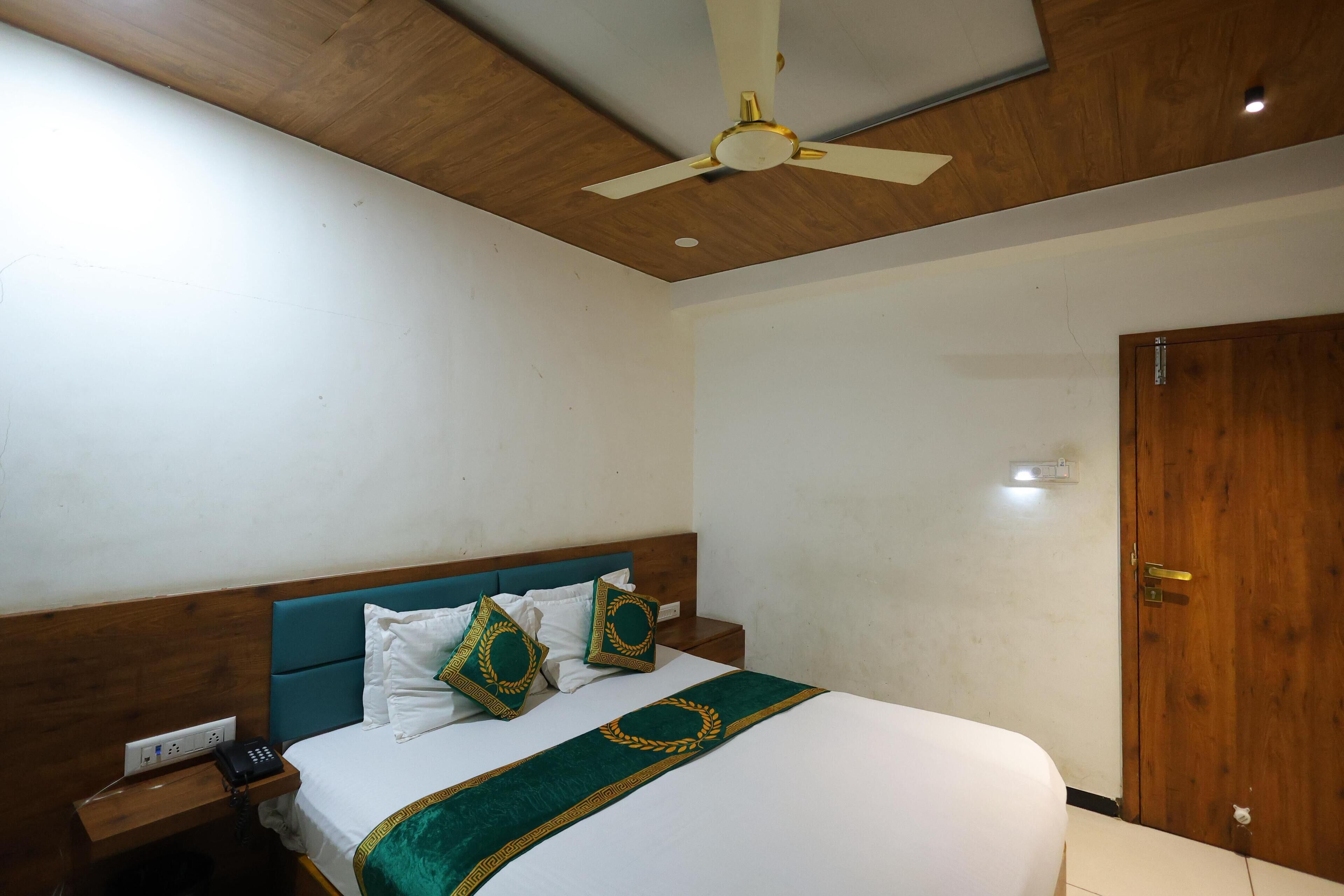 A hotel room with a wooden ceiling, a bed with white bedding and decorative pillows, a bedside table with a phone, and a wooden door.