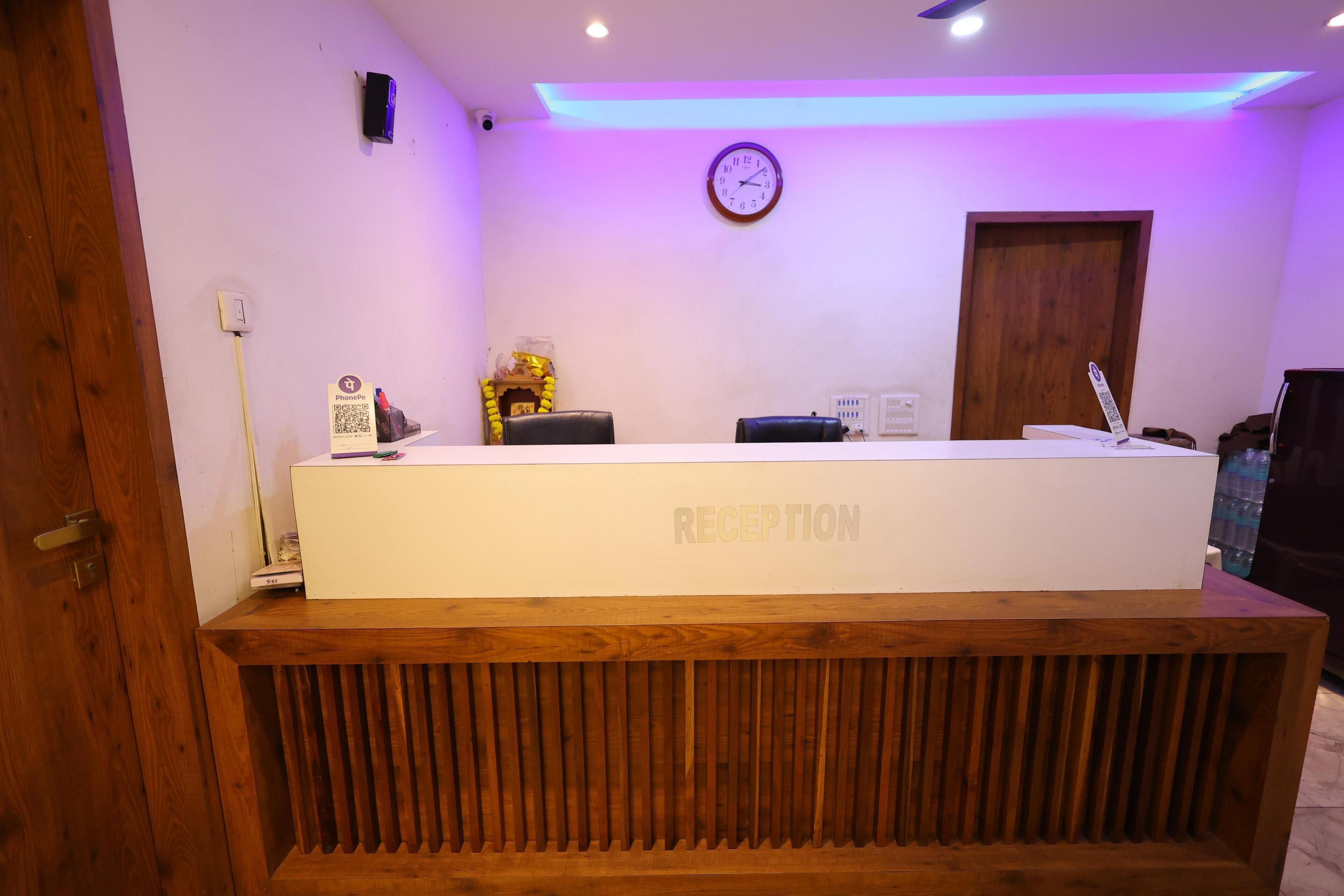 A reception desk with a wooden base and a white top, a clock on the wall, and a door to the right.