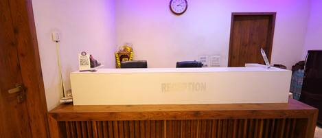 A reception desk with a wooden base and a white top, a clock on the wall, and a door to the right.