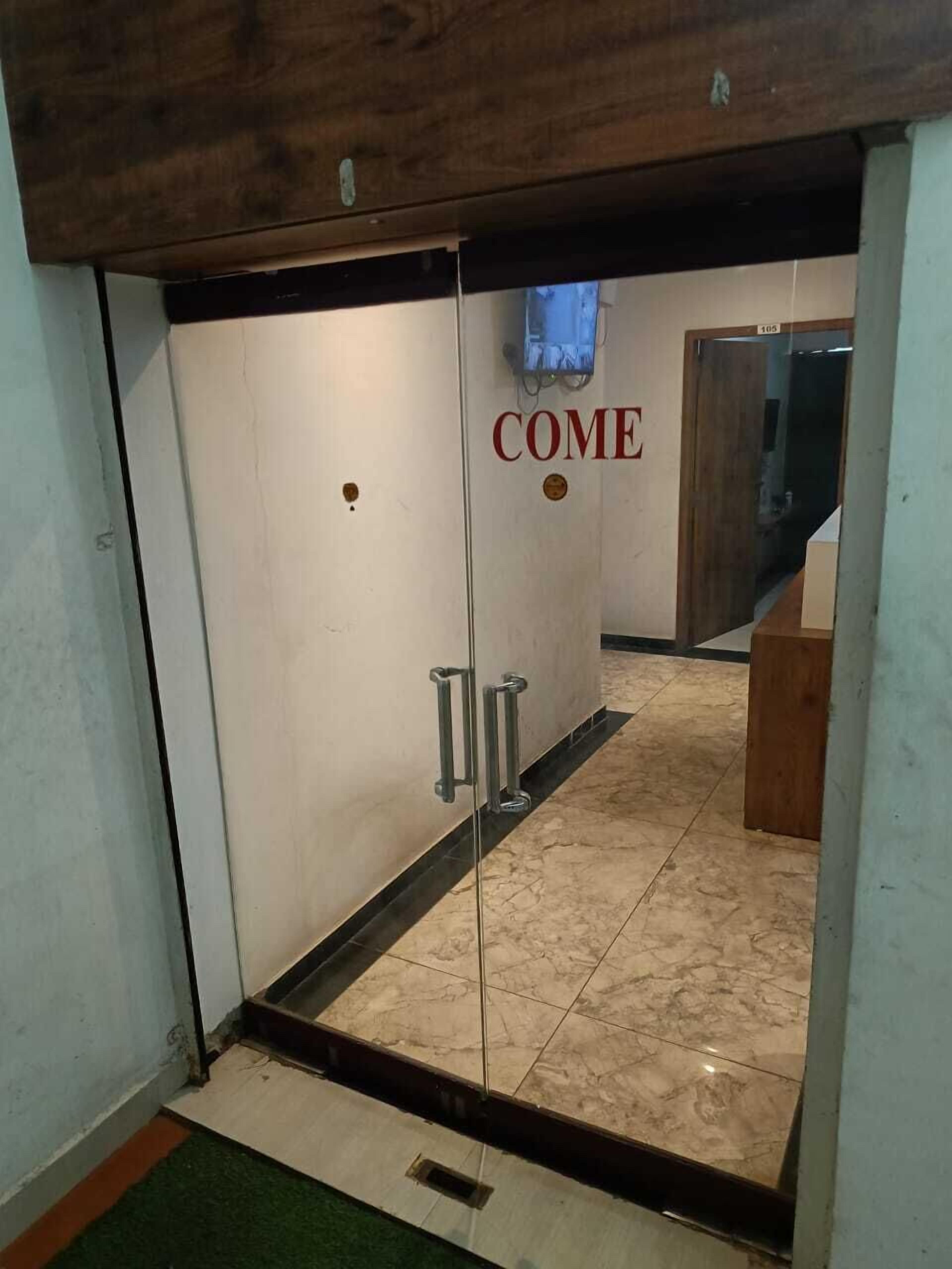 A hotel entrance with a 'COME' sign, a wooden ceiling, and a tiled floor.