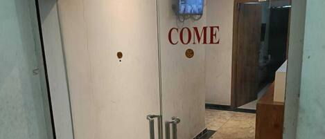 A hotel entrance with a 'COME' sign, a wooden ceiling, and a tiled floor.