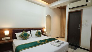 A hotel room with a bed, nightstands, a mirror, an air conditioning unit, and a door. - Hotel Royal Raj (Rajkot)