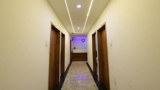 A hallway with a marble floor, wooden doors, and a reception desk with a clock on the wall. - Hotel Royal Raj (Rajkot)
