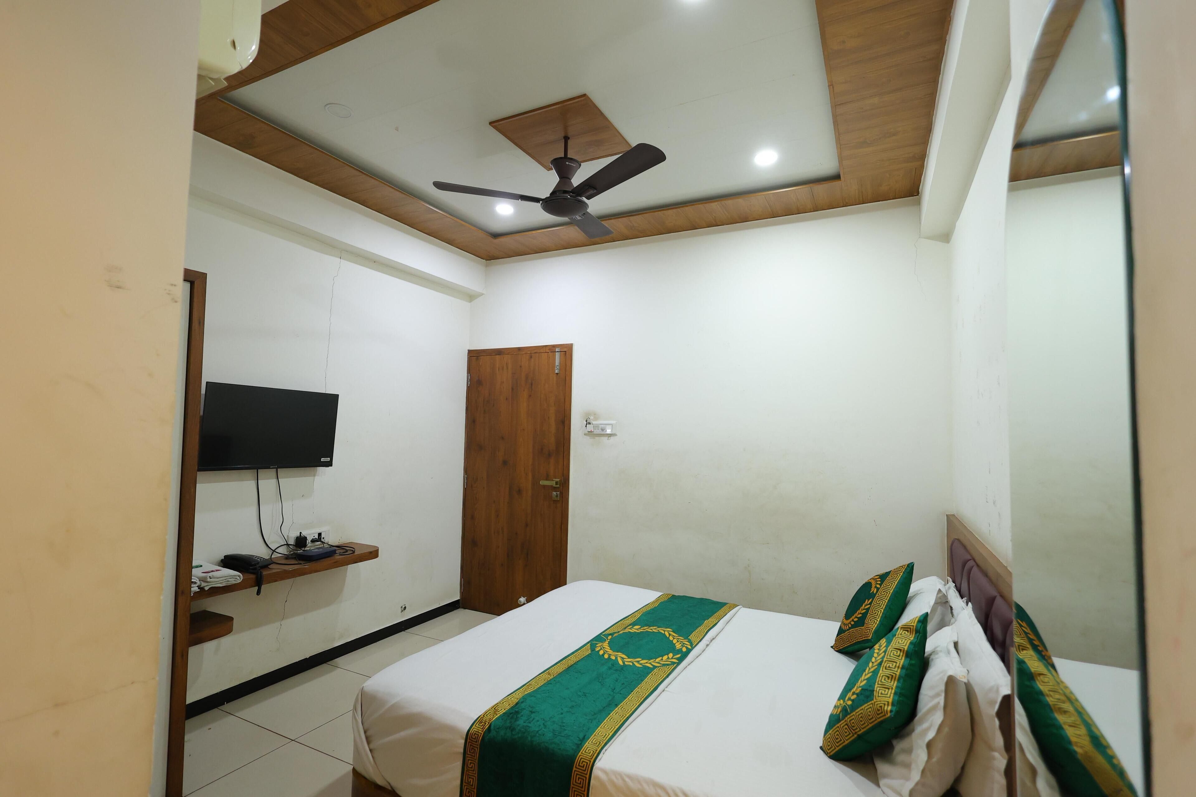 A bedroom with a bed, a ceiling fan, a TV on the wall, and a wooden door.