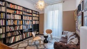A cozy living room with a large bookshelf, a comfortable sofa, a wooden chair, and a decorative chandelier. - The Designer's Flat by Wonderful Italy (Genoa)