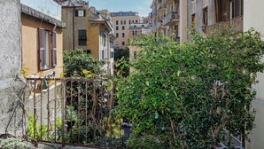 A narrow urban street with buildings on both sides, featuring balconies and a dense green shrubbery in the foreground. - The Designer's Flat by Wonderful Italy (Genoa)