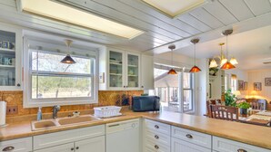 Una cocina con armarios blancos, un lavamanos, un microondas y una ventana.