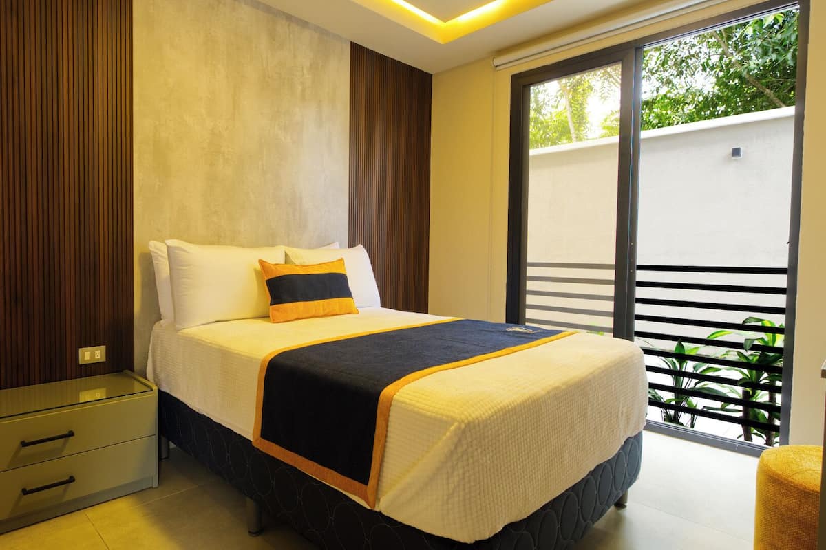 A modern bedroom with a bed, bedside tables, and a view of greenery outside.