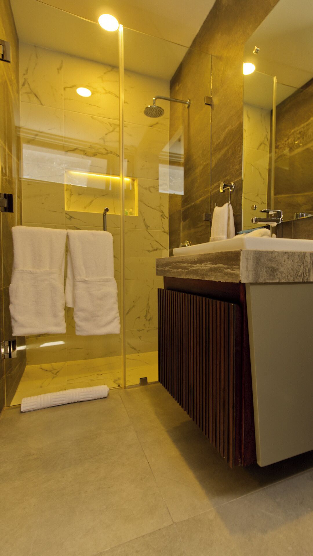 A modern bathroom with a glass-enclosed shower, a vanity with a marble countertop, and two towels hanging on the wall.