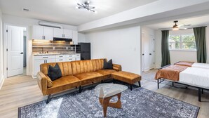 Habitació moderna i ben il·luminada amb sofà, taula de café de vidre, llit i petita cuina.