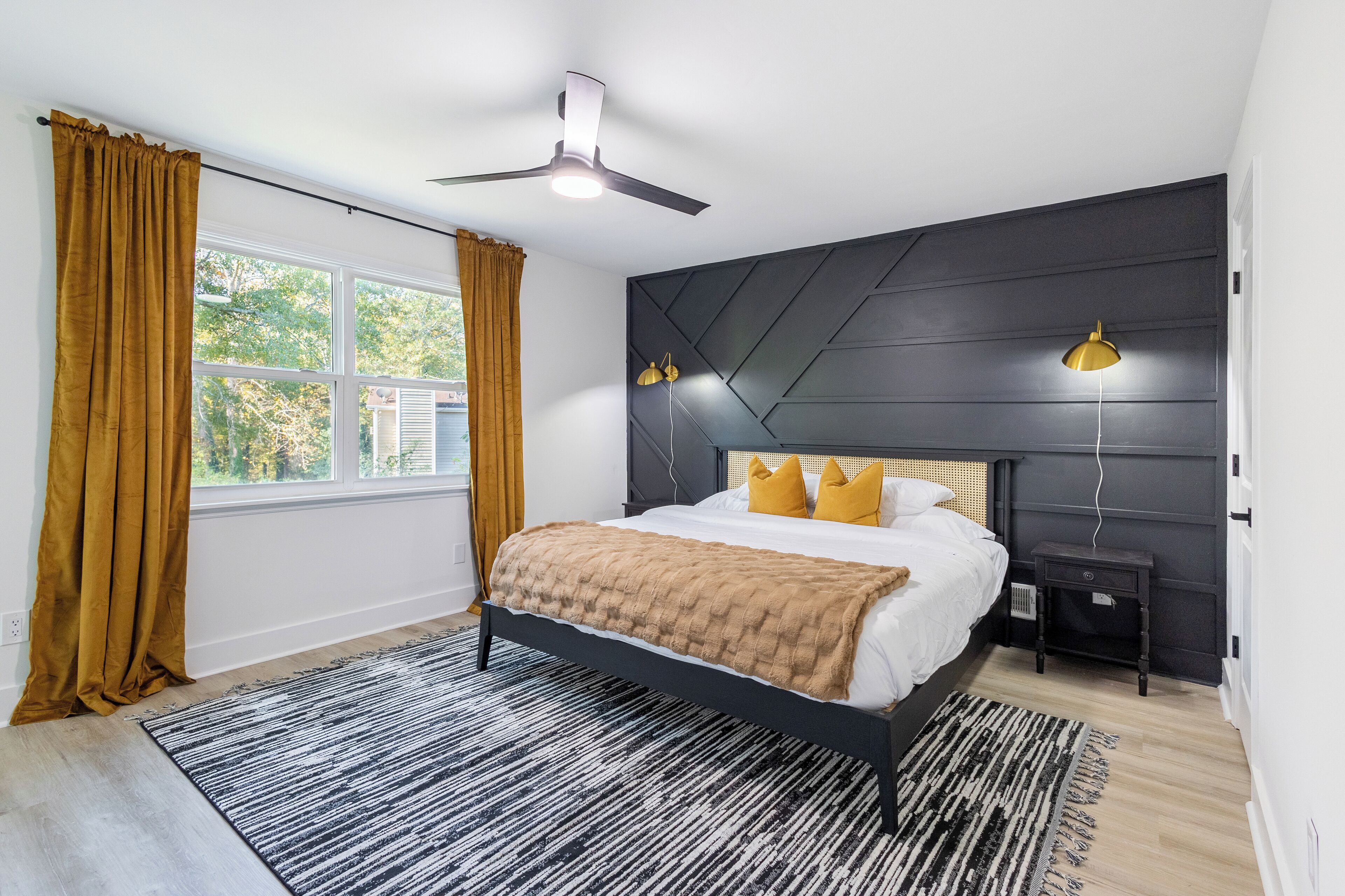 A modern bedroom with a bed, a ceiling fan, a nightstand, and a window with curtains.