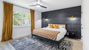 Une chambre moderne avec un lit, un ventilateur de plafond, une table de chevet et une fenêtre avec des rideaux.