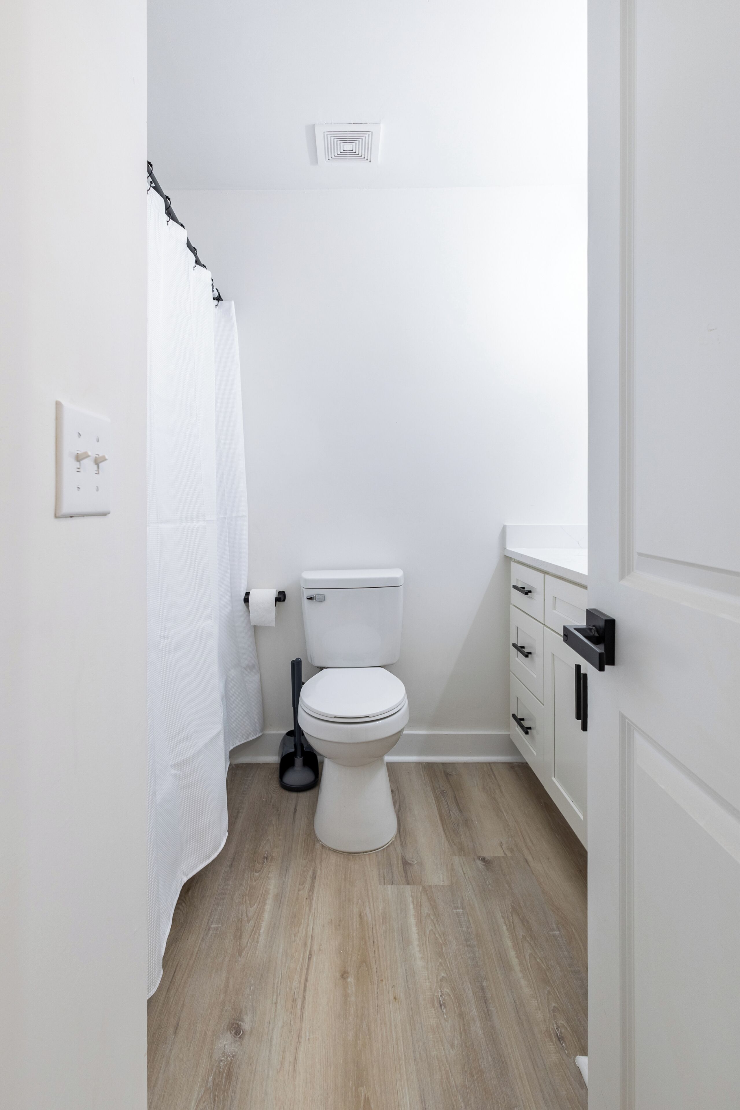 Une petite salle de bain blanche, avec des toilettes, un rideau de douche et un plancher en bois.