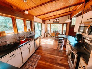 A rustic kitchen with wooden beams, a large island, and a view of the outdoors.