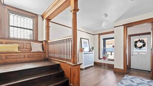 Una escalera de madera con barandilla, un banco con cojines, un radiador y una puerta adornada con un adorno navideño.