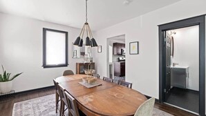 Un comedor con una mesa de madera, sillas, una araña y vista a la cocina.