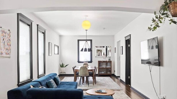 Una sala moderna con un sofá azul, un comedor con una mesa y sillas, y un televisor montado en la pared.