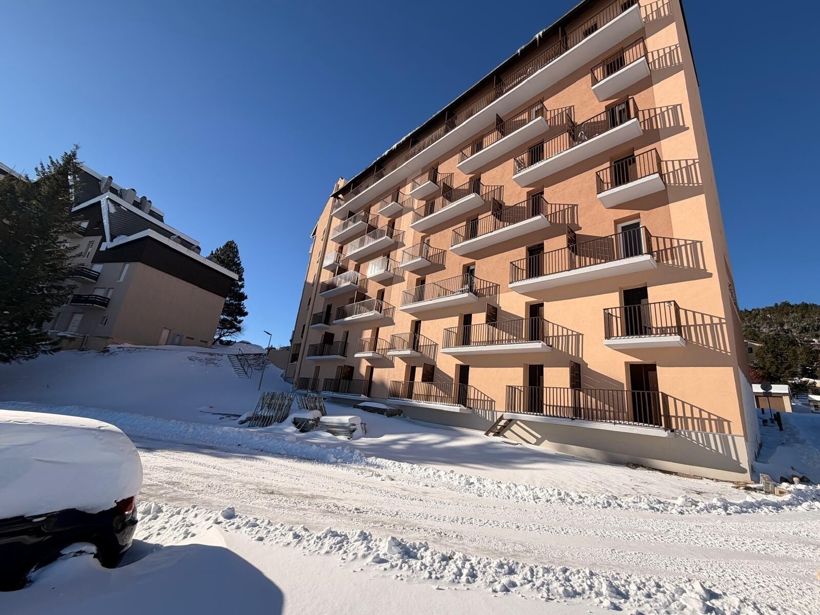 Un immeuble à plusieurs étages doté de balcons, un sol recouvert de neige et un ciel dégagé.
