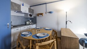 Ett kompakt kök med ett matbord för fyra personer, utrustat med grundläggande köksapparater och en enkel hängande lampa.