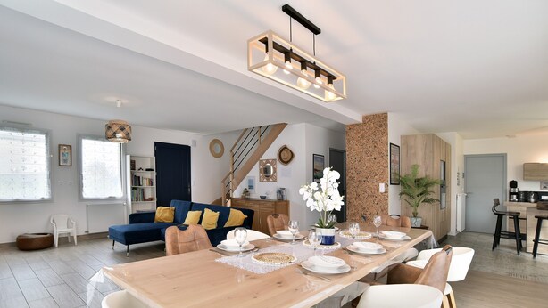 Uma sala de estar moderna com área de jantar, apresentando uma mesa de jantar de madeira posta para quatro pessoas, um sofá azul e uma escada que leva a outro nível.