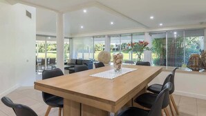 A spacious dining area with a wooden table and black chairs, large windows offering a view of greenery, and a modern interior design.