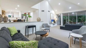 A spacious living area with a high ceiling, a sofa set, a coffee table, and a TV.
