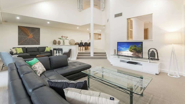 A modern living room with a black leather sofa, a glass coffee table, and a flat-screen TV on a white entertainment unit.