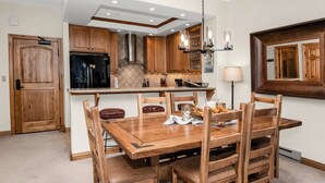 Zona pranzo con tavolo e sedie in legno, cucina con mobili in legno, frigorifero nero e un lampadario.