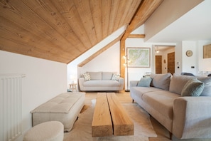 Ein gemütliches Wohnzimmer mit hoher Holzbalkendecke, einer Sofagarnitur, einem Couchtisch und einer Heizung.