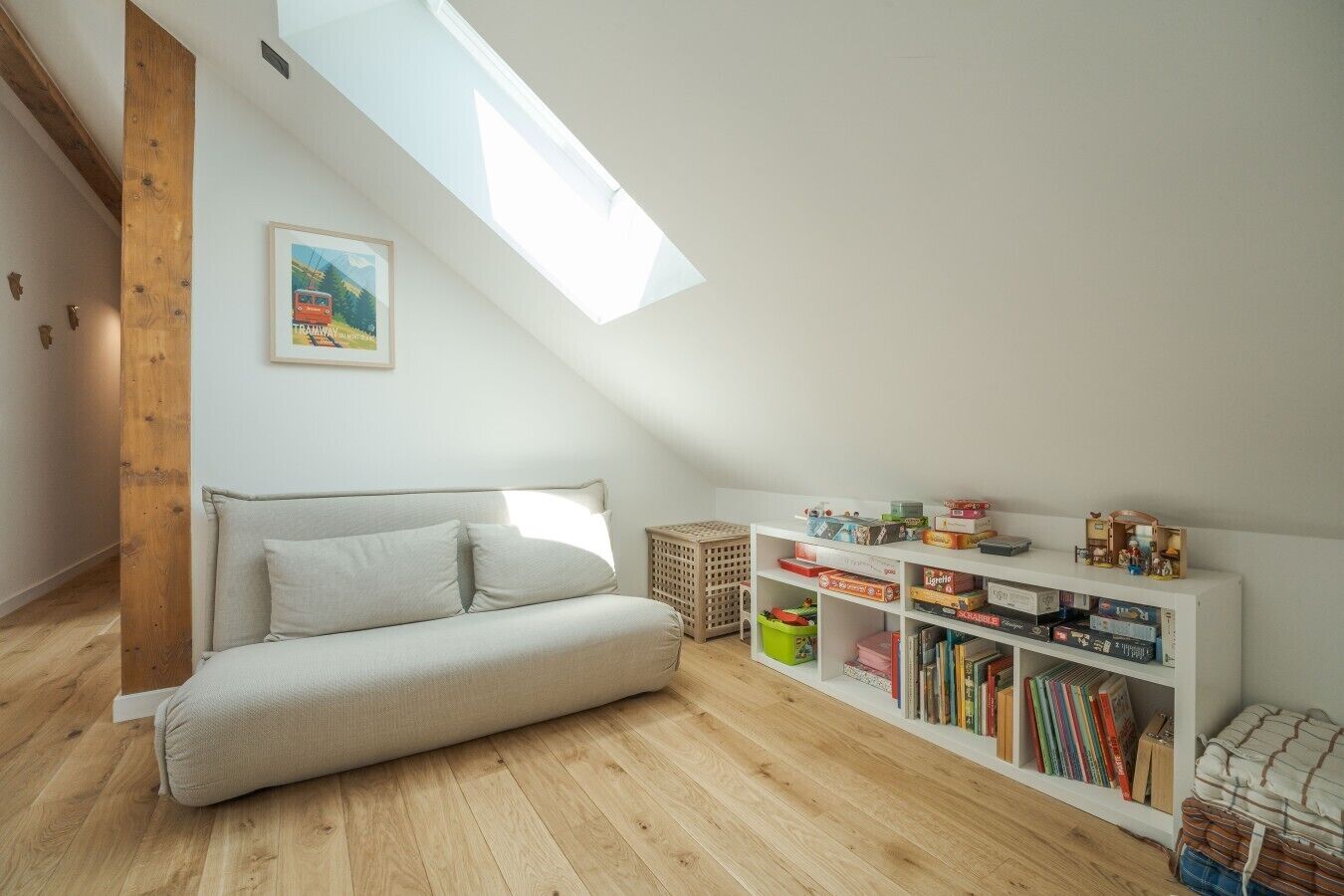 Dormitorio tipo loft con techo inclinado, sofá, estantería y tragaluz.