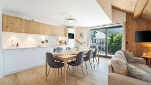 Een moderne keuken met witte kastjes, een eettafel gedekt voor vier personen, en een grote schuifpui die leidt naar een balkon met uitzicht op groen.