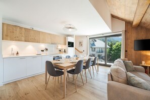 Eine moderne Küche mit weißen Schränken, einem Esstisch für vier Personen und einer großen Schiebeglastür, die auf einen Balkon mit Blick ins Grüne führt.