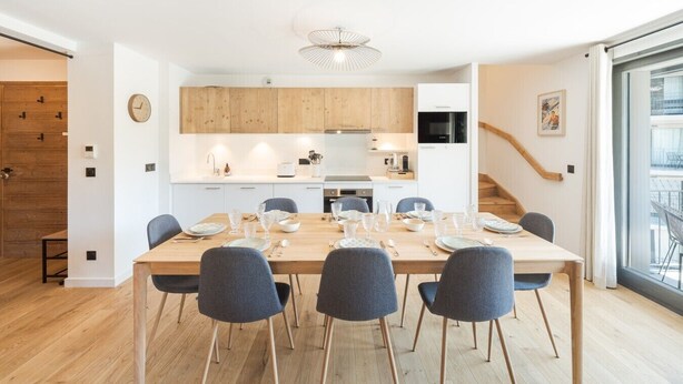 Een moderne keuken met houten kastjes, een eethoek met een tafel voor zes personen, en een trap naar een bovenverdieping.