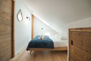 A room with a bed, wooden walls, a skylight, and a hanging mirror.