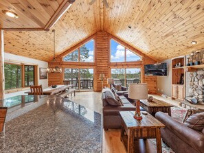 Un intérieur spacieux de chalet en bois, comprenant une grande salle à manger, un salon avec cheminée et un mur décoratif en pierre.