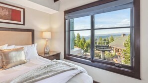 Una habitació d'hotel amb una finestra gran, un llit amb roba blanca, una tauleta de nit amb una làmpada i un quadre amb marc a la paret.