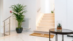 Un hall d’hôtel moderne avec un sol en marbre, une plante en pot, une table en verre agrémentée d’un objet décoratif, un paillasson et un escalier.