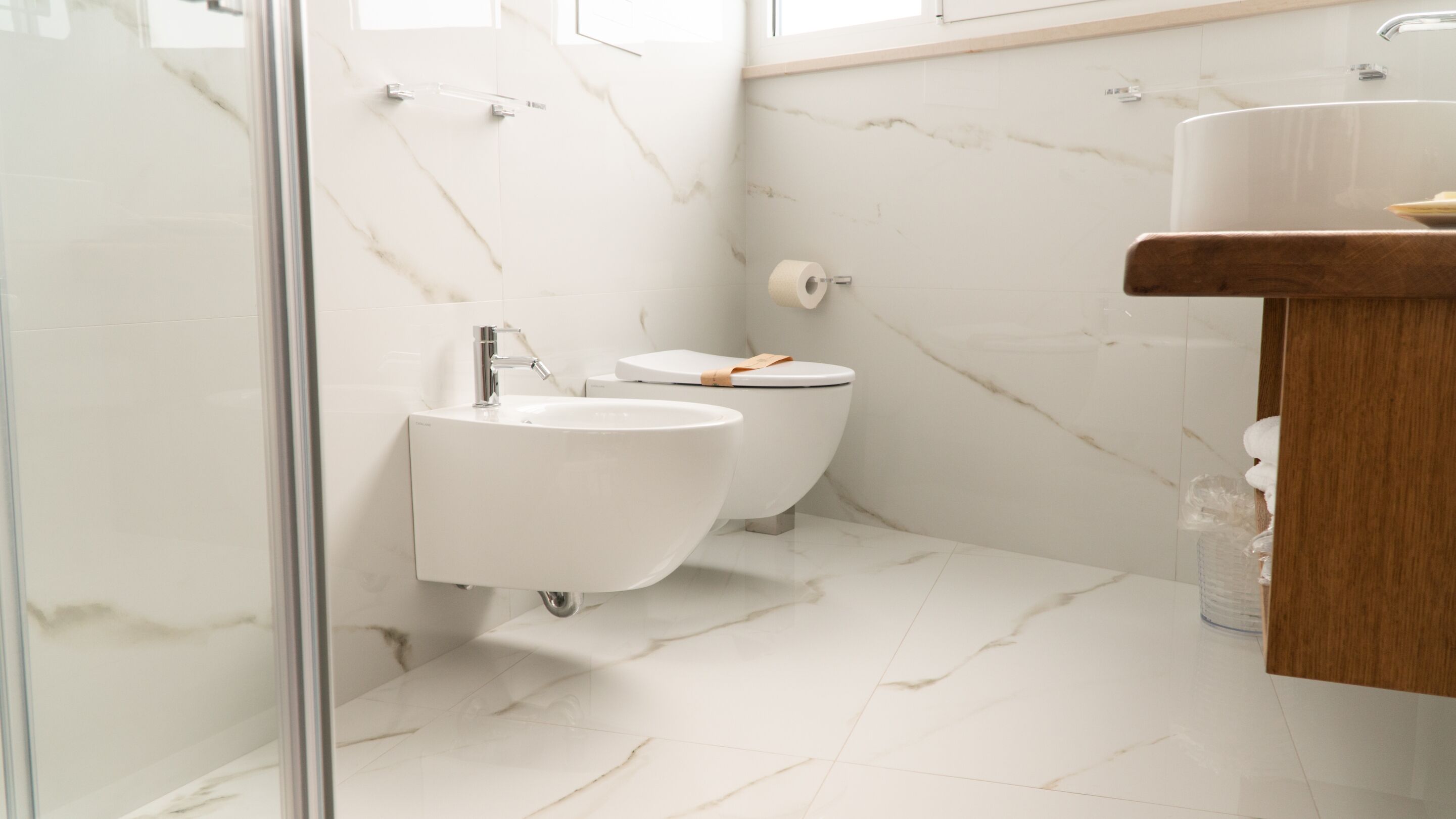 A bathroom with a glass shower enclosure, a white sink, and a toilet.