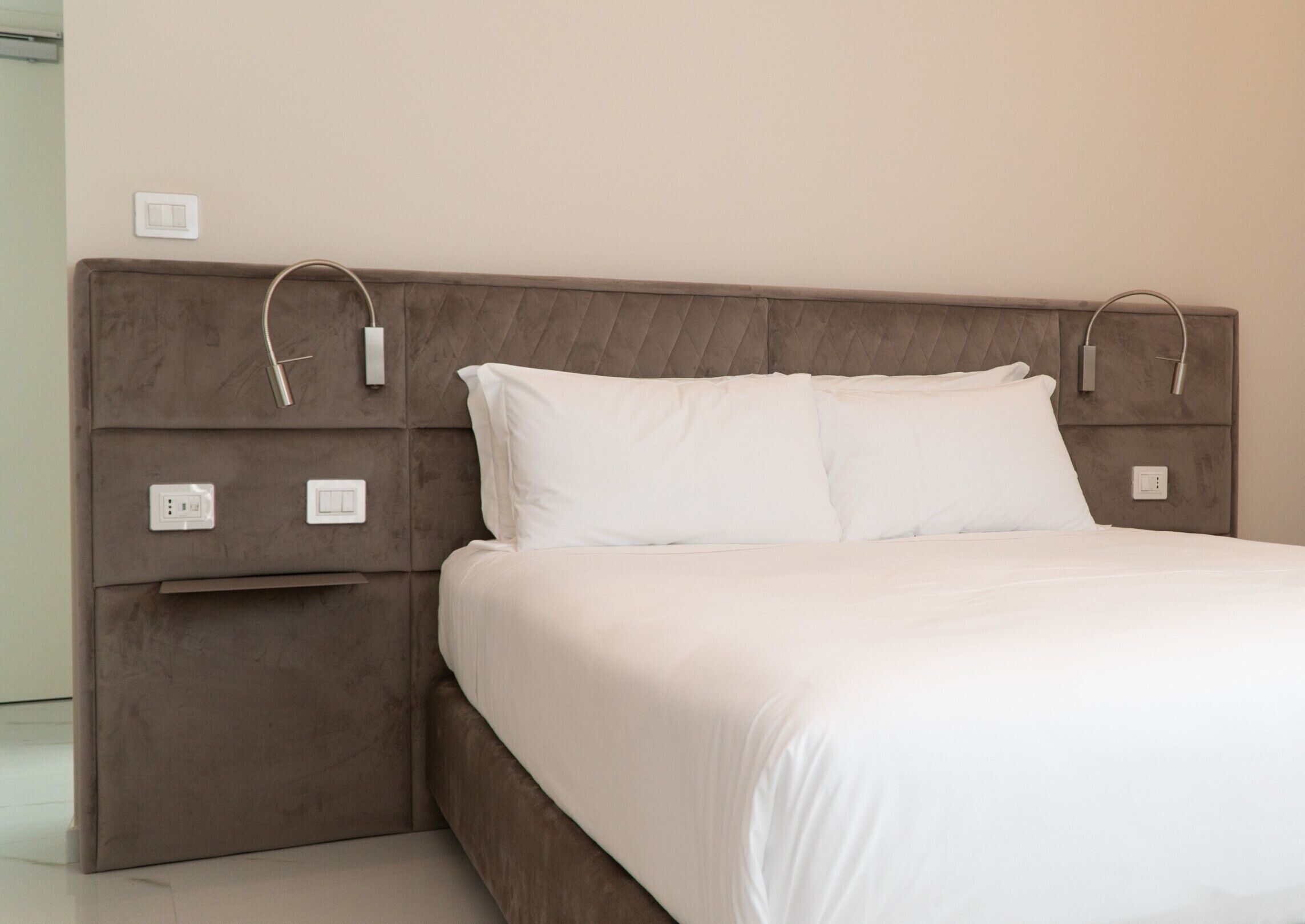 A modern bedroom with a large bed, a headboard with integrated charging ports, and a bedside table with a power outlet.